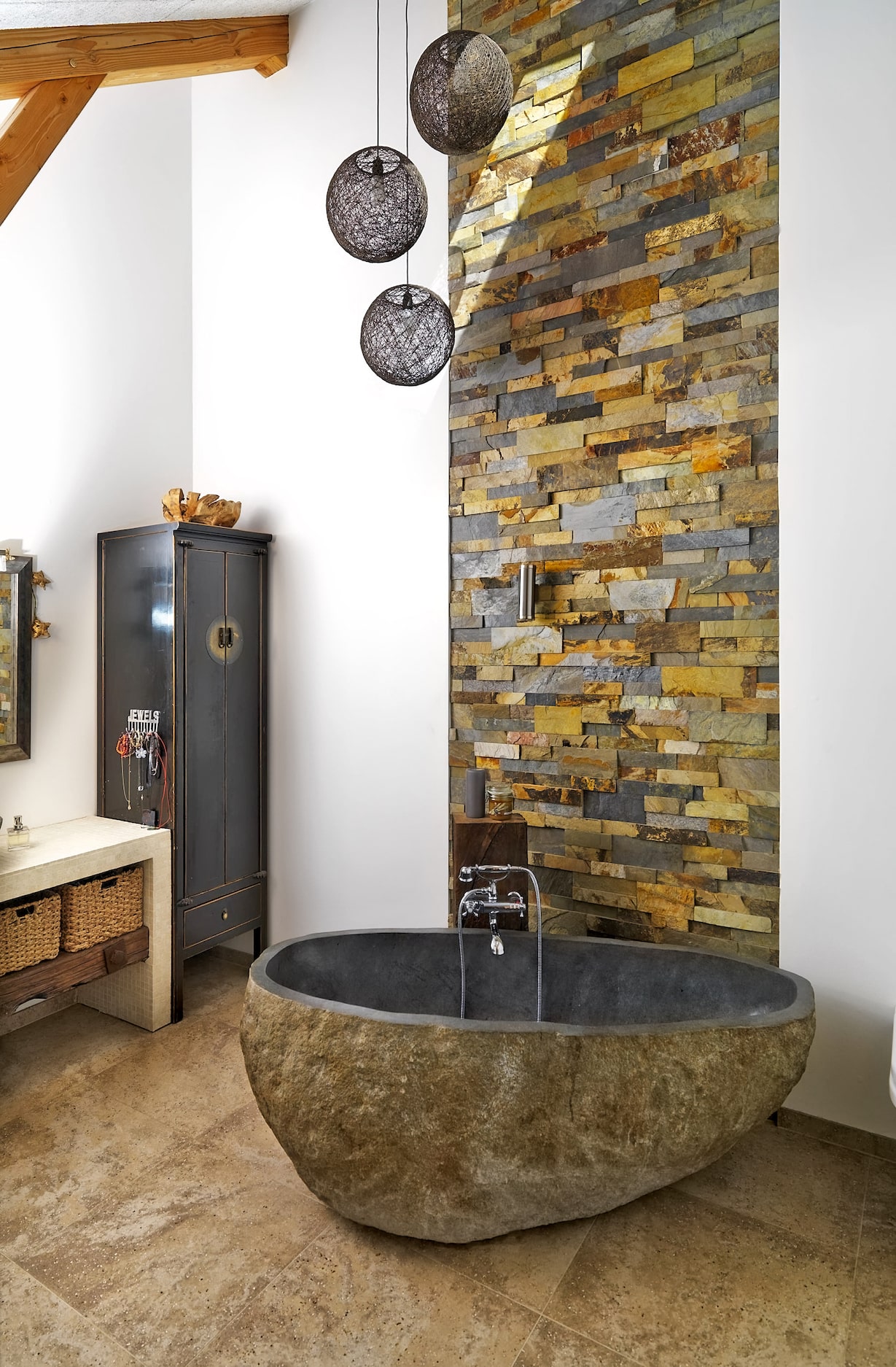 A super unique stone bathroom featuring a floor to ceiling stacked stone feature wall and a freestanding one piece natural stone tub.